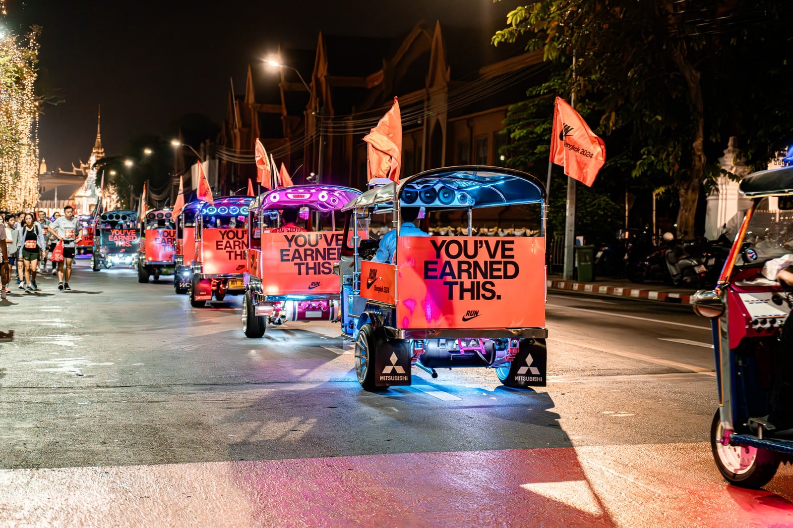 Nike 'You've Earned This' neon-lit tuk-tuk convoy at night in Bangkok, printed and installed by Bigger Ads