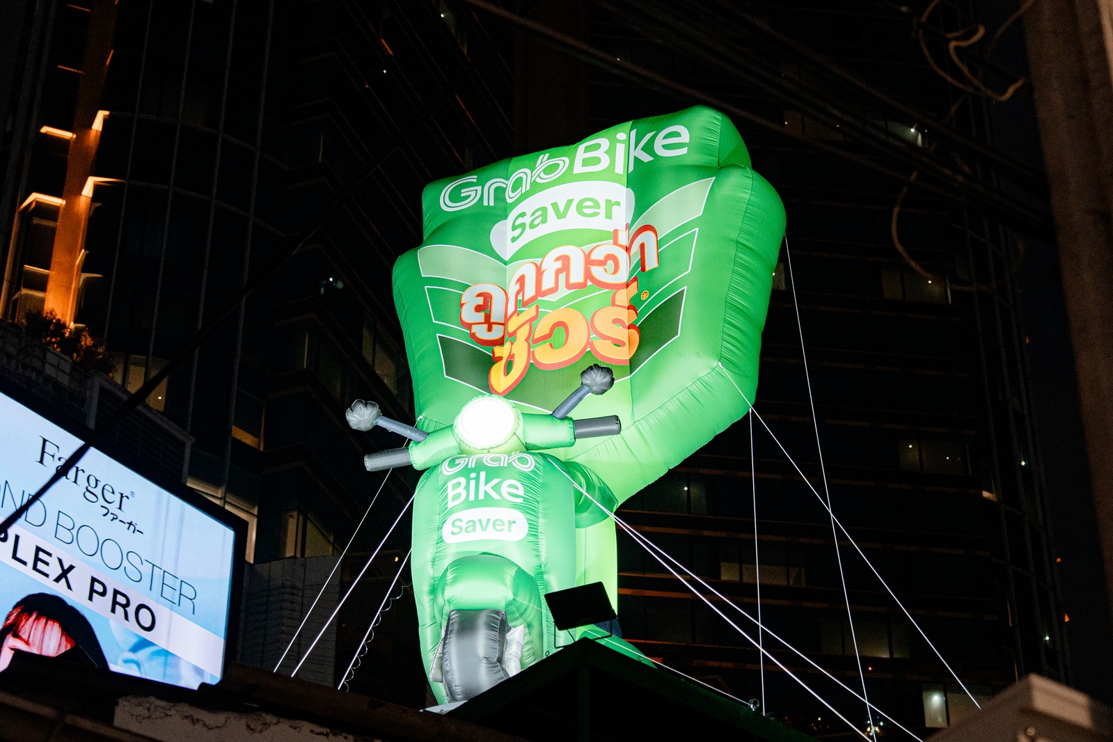 Giant glowing green GrabBike inflatable scooter mounted above a night street