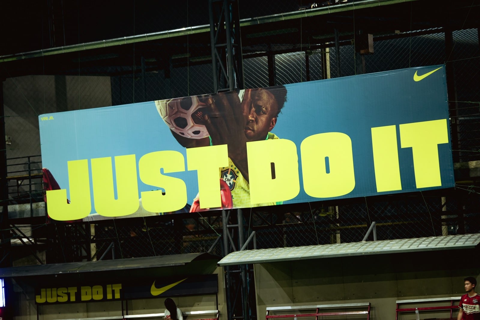 Nike JUST DO IT billboard in lime type over blue at a floodlit futsal pitch at night