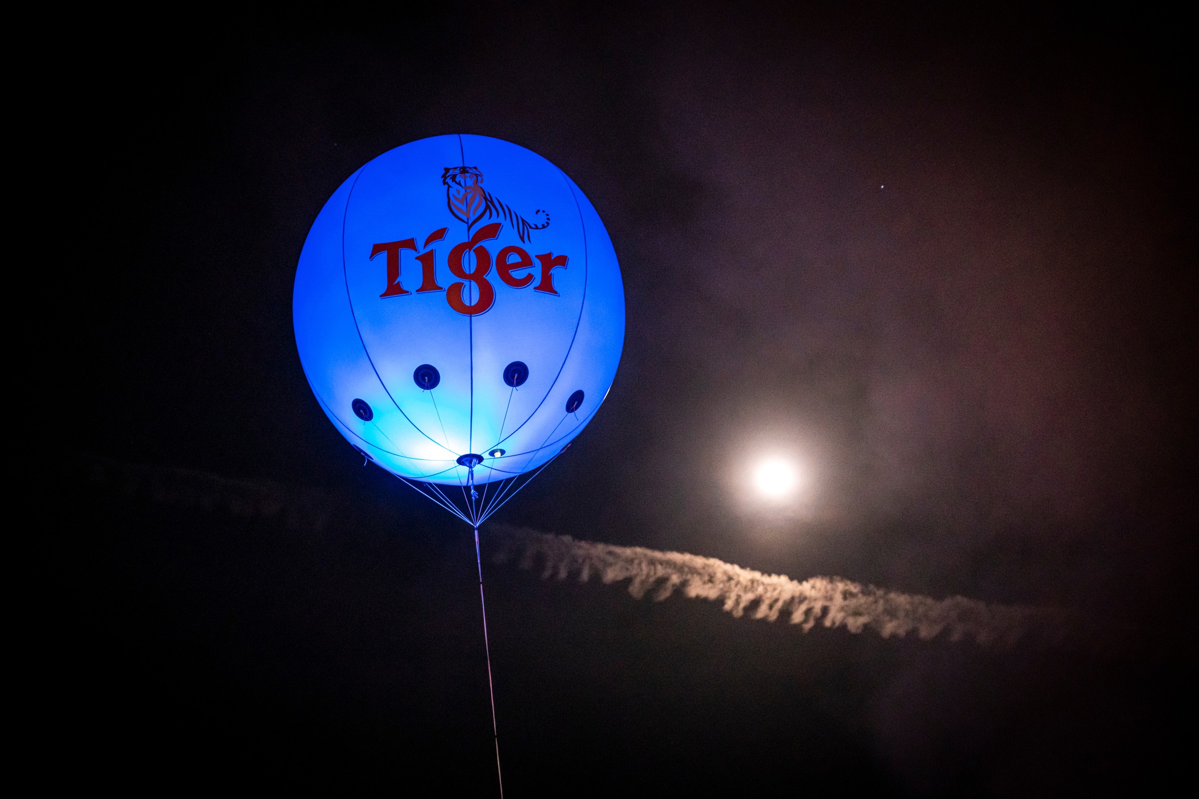 Illuminated blue Tiger beer balloon floating beside a full moon at night
