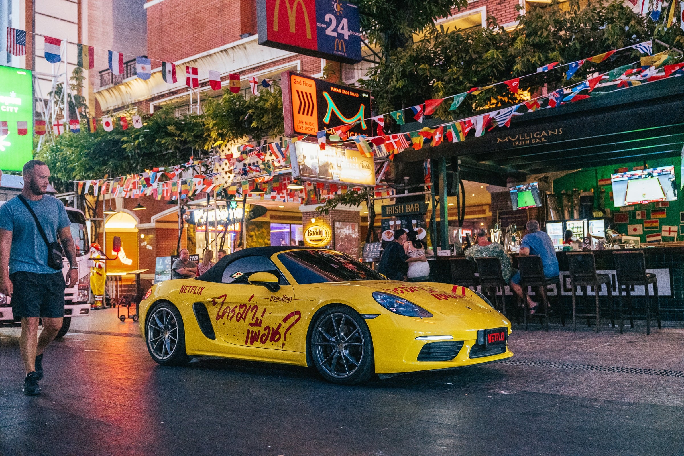 Yellow Netflix-wrapped Porsche parked on Khaosan Road at dusk